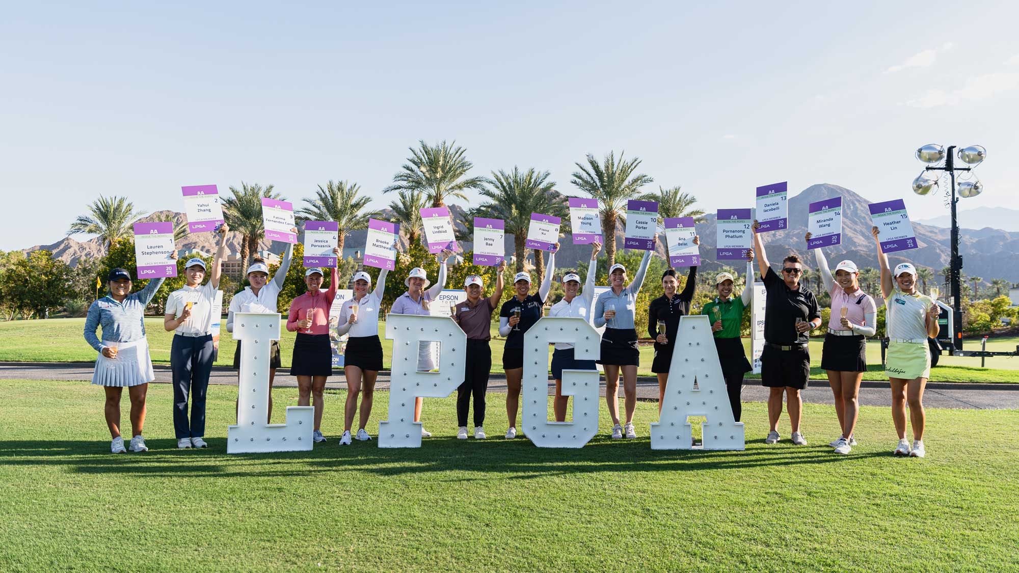 Women golfers pose behind large LPGA letters on a sunny green golf course.