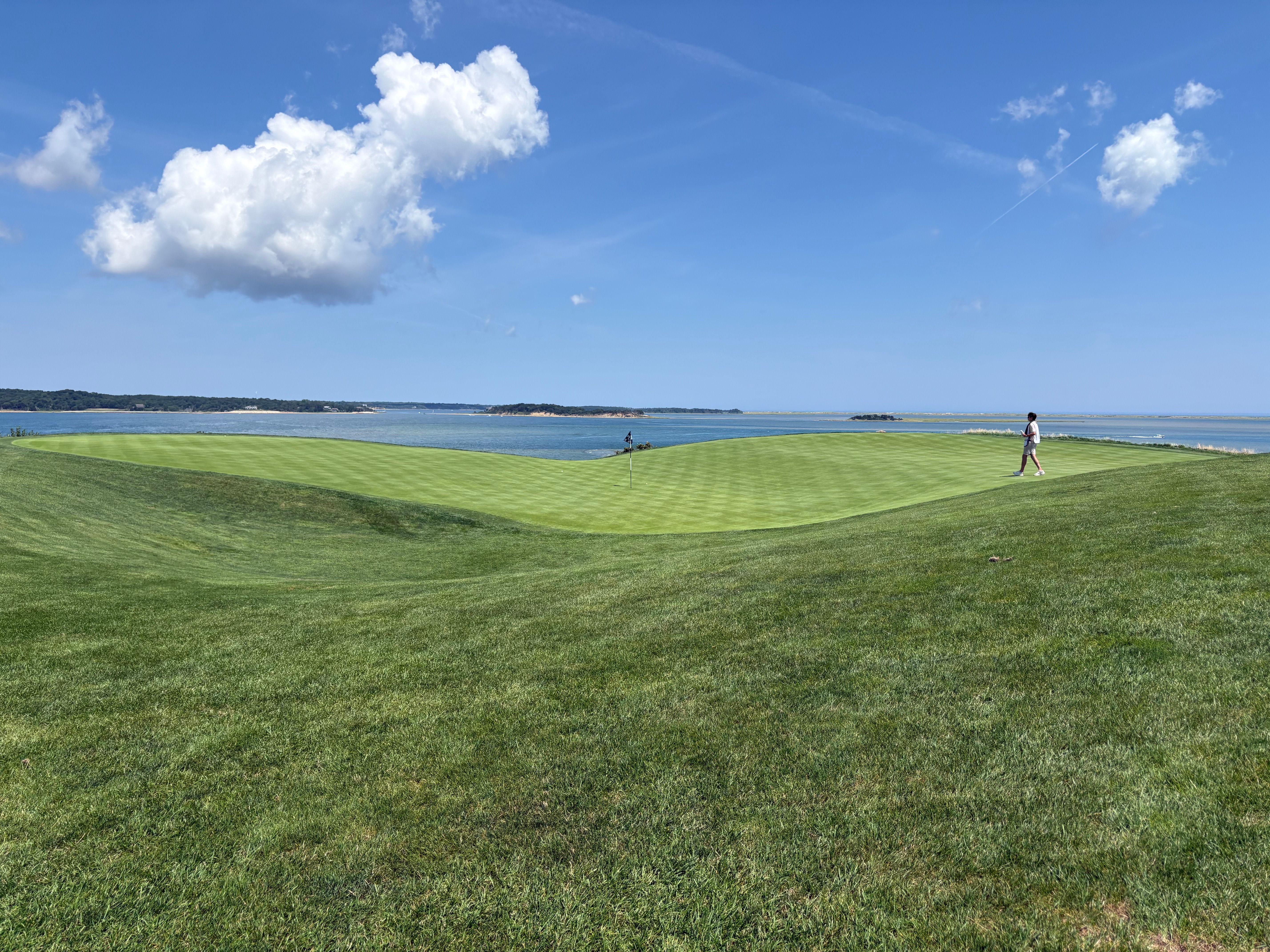 Lush green golf course beside a blue ocean under a partly cloudy sky.