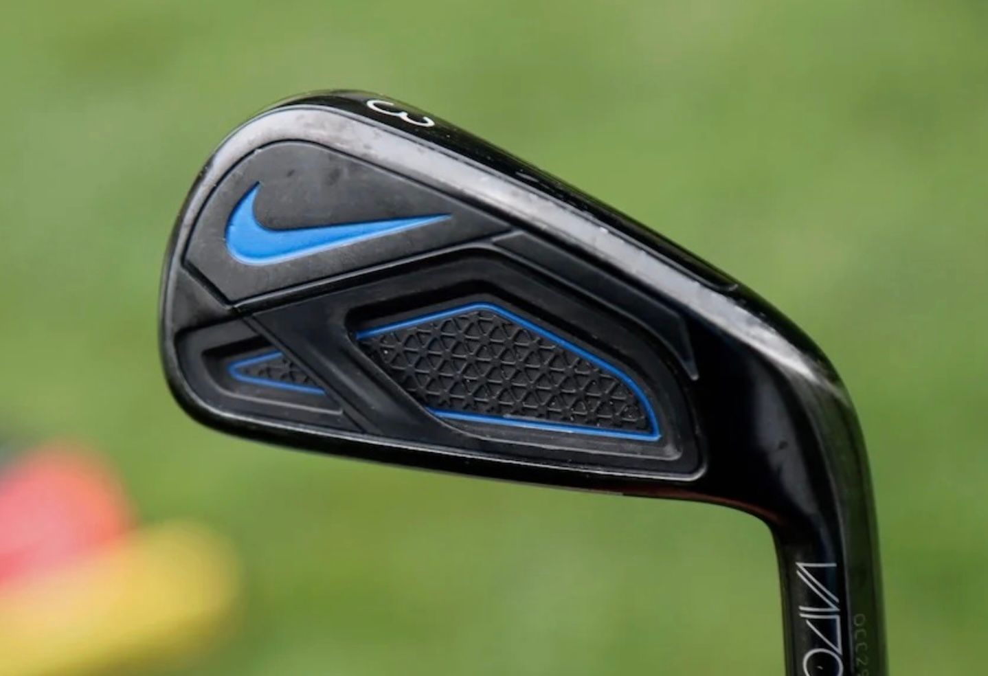 Close-up of a black Nike golf club iron featuring a blue swoosh logo and accents.