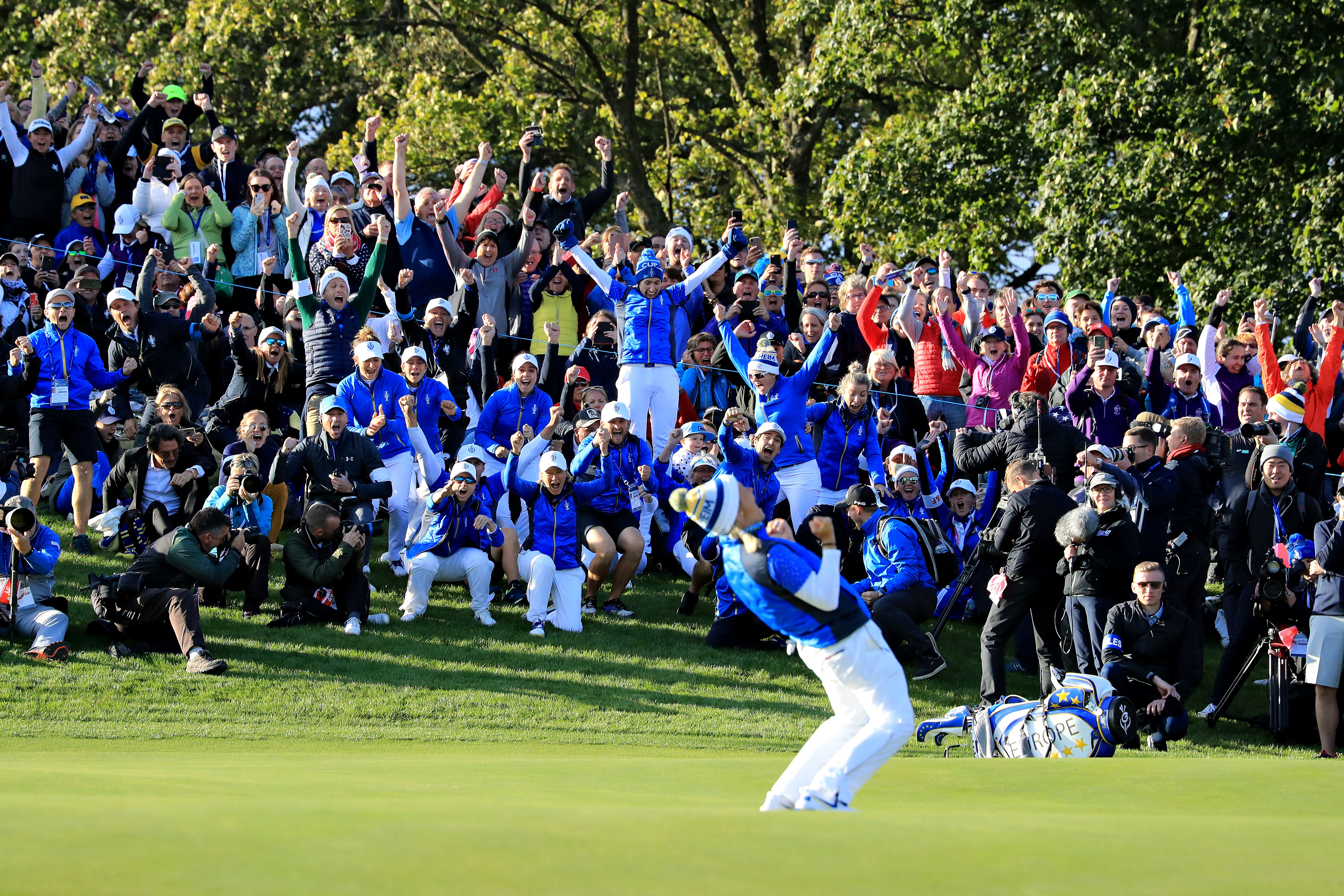 Golfer in blue and white celebrates dramatically on a green course with cheering crowd.