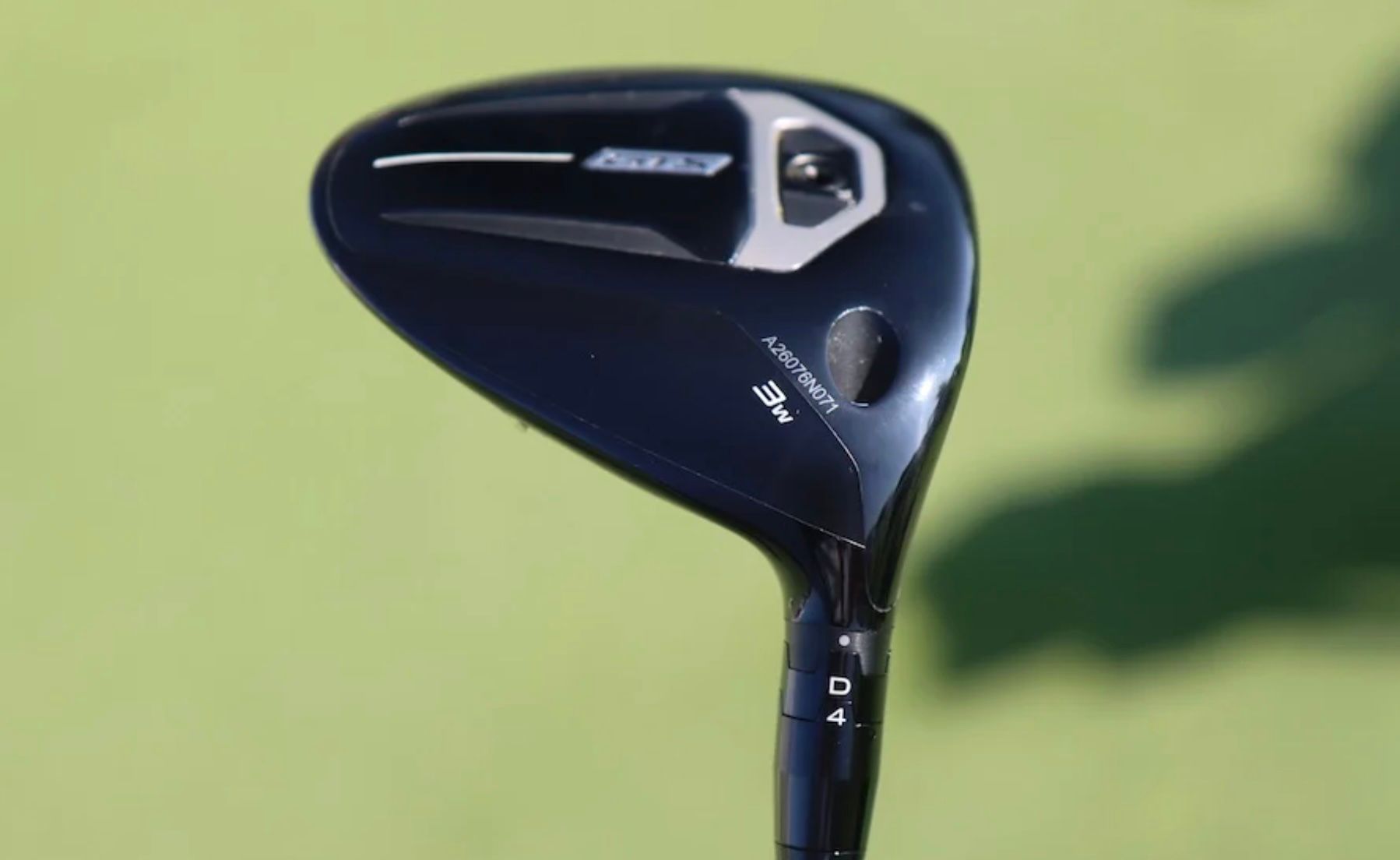 Sleek black golf club head with white and silver details on a green fairway.