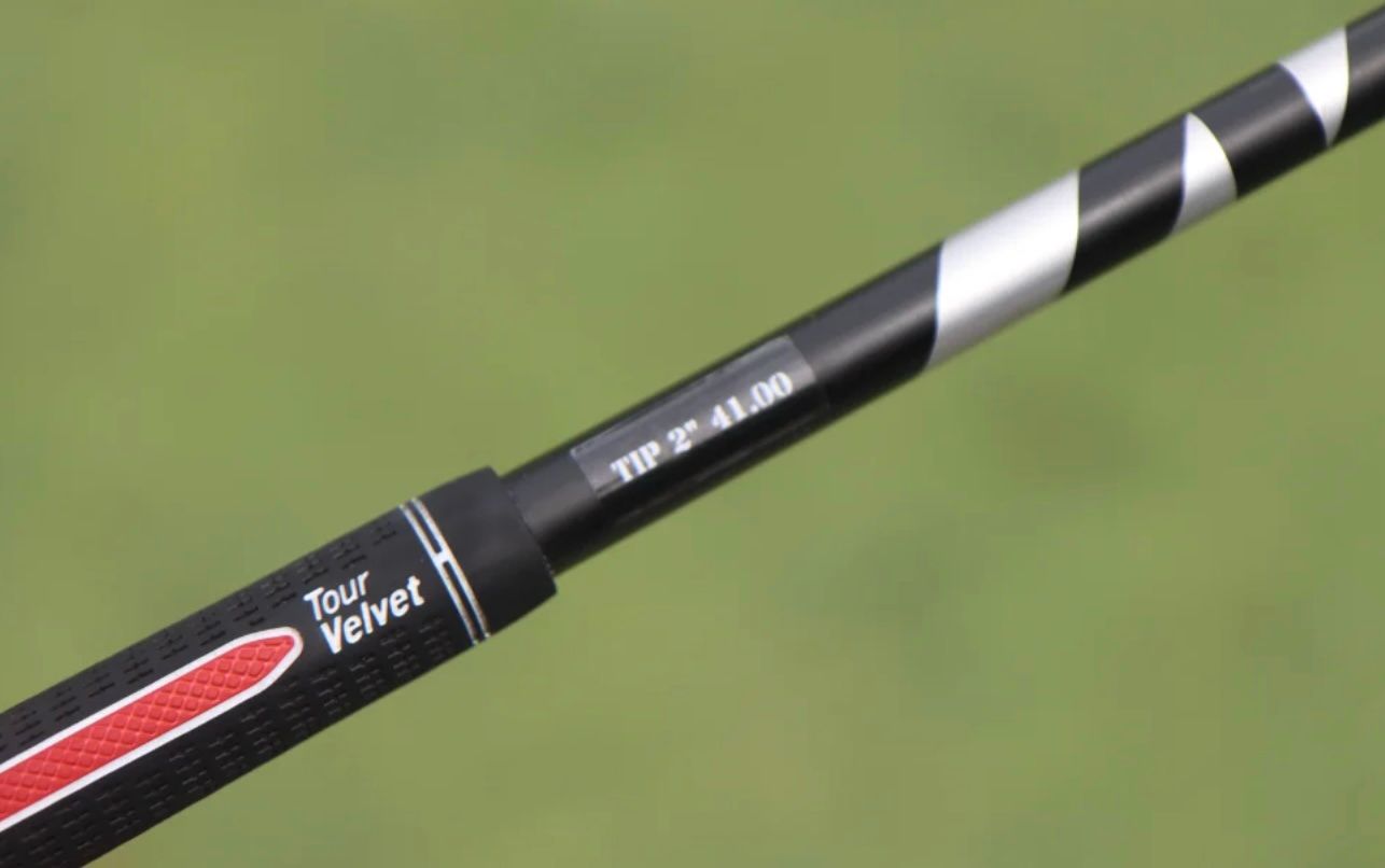 Close-up of a black golf club grip with 'Tour Velvet' and a striped graphite shaft.
