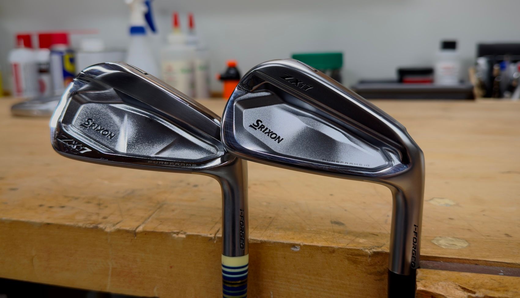 Two sleek, modern golf irons with shiny clubheads on a wooden workbench.
