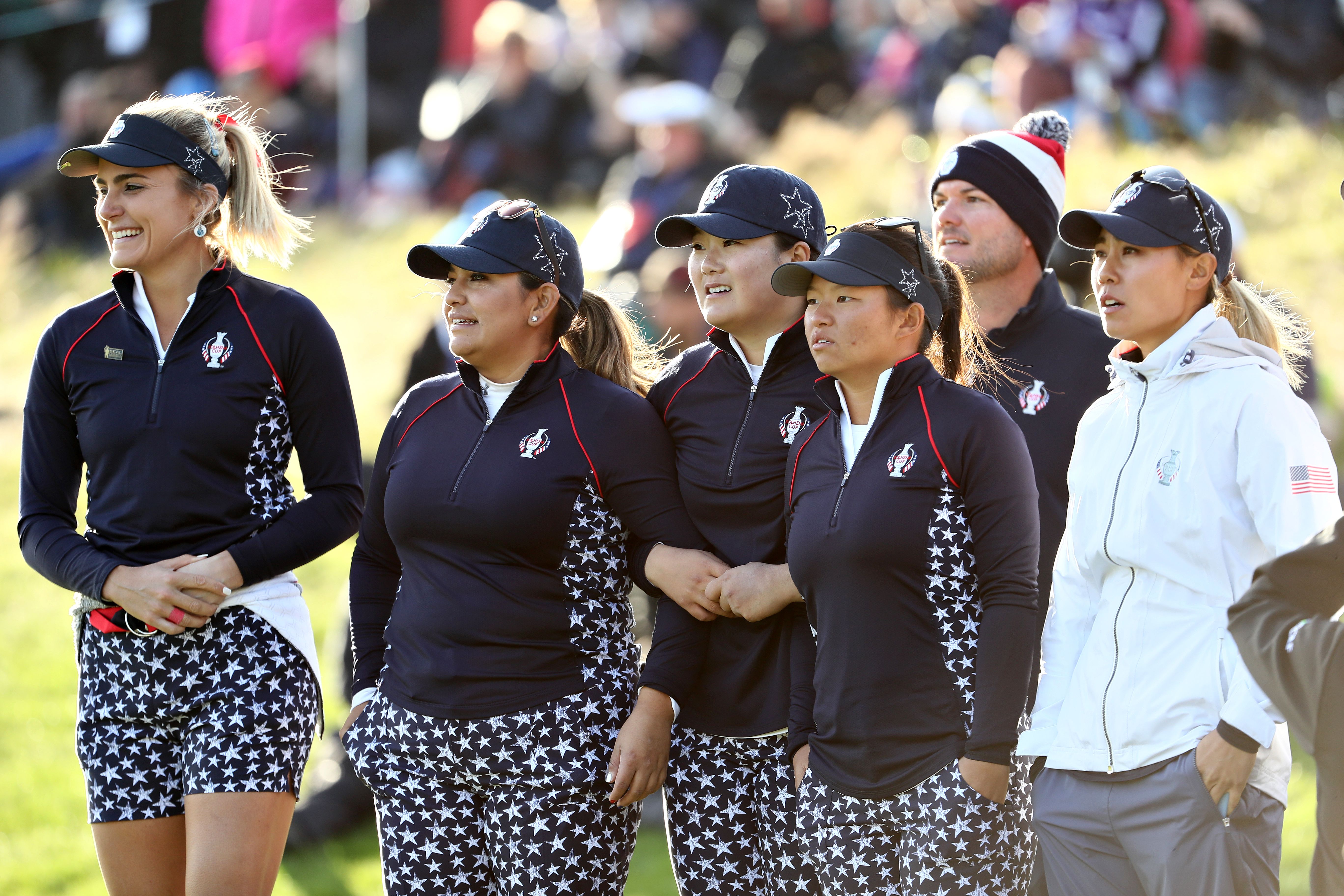 A group of female golfers in matching navy uniforms and patterned shorts stand outdoors.