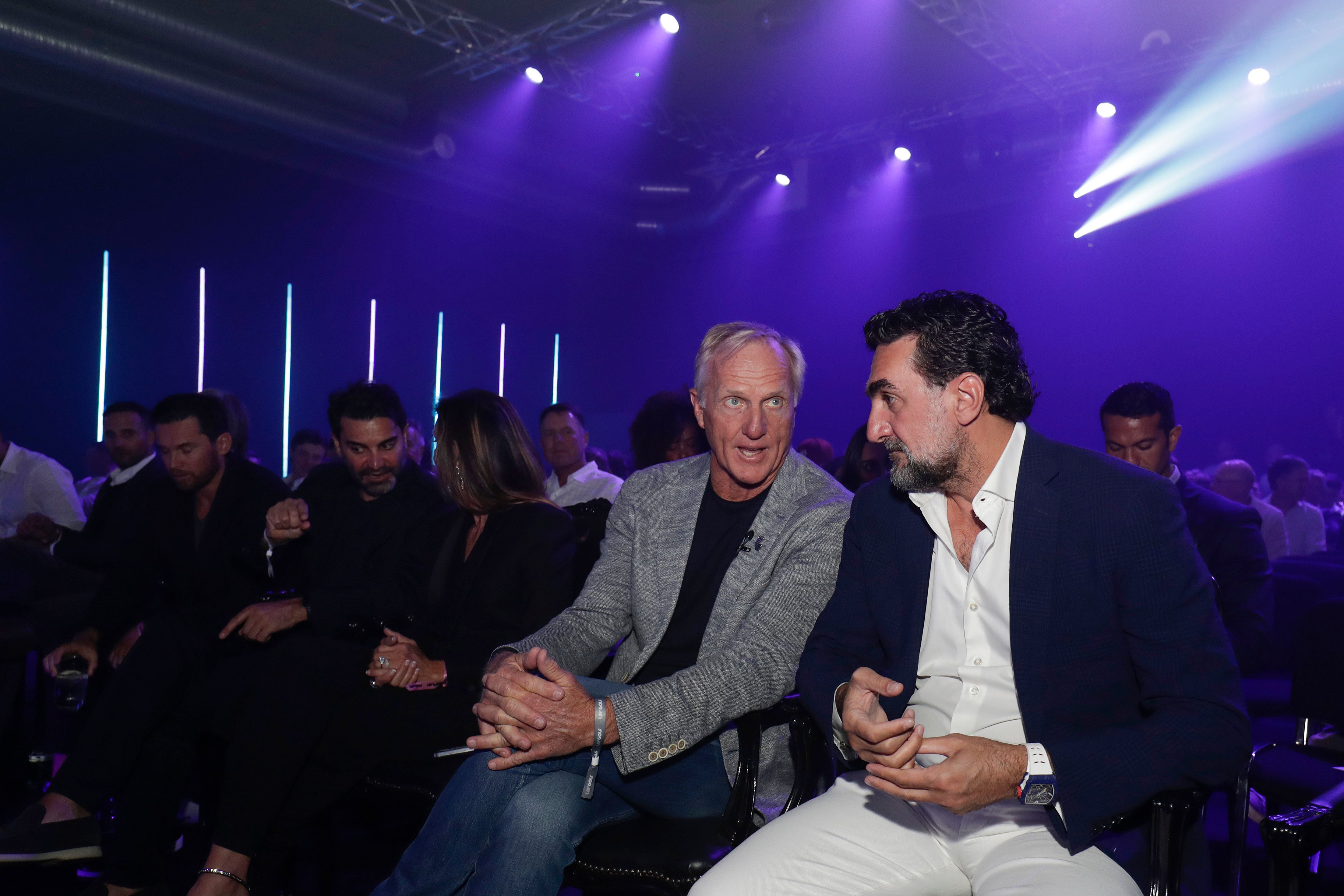 Two men in suits talking intently at a dimly lit event.
