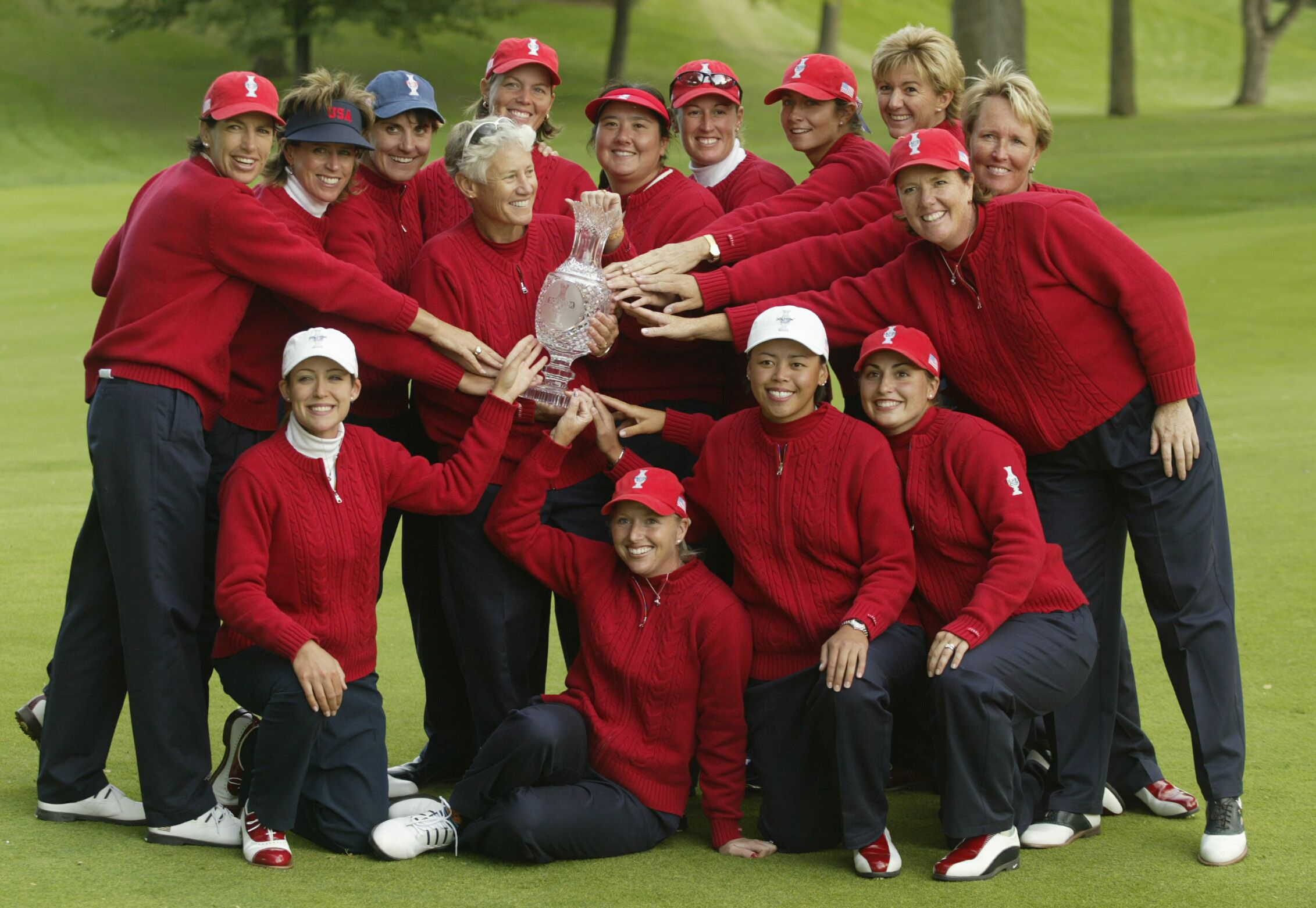A group of women golfers in red sweaters celebrates with a championship trophy.