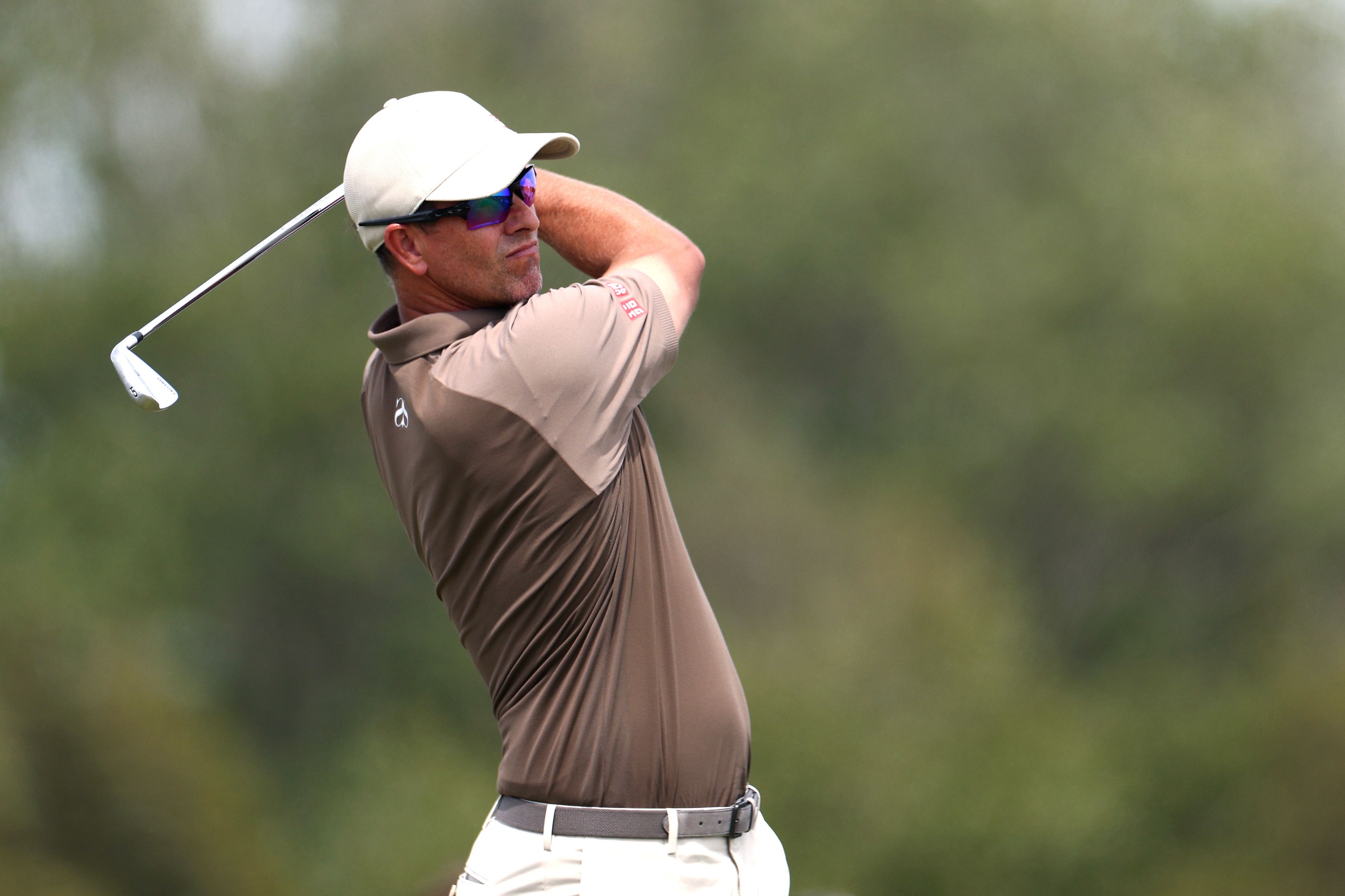 Male golfer in white cap and sunglasses mid-swing with a club on a golf course.