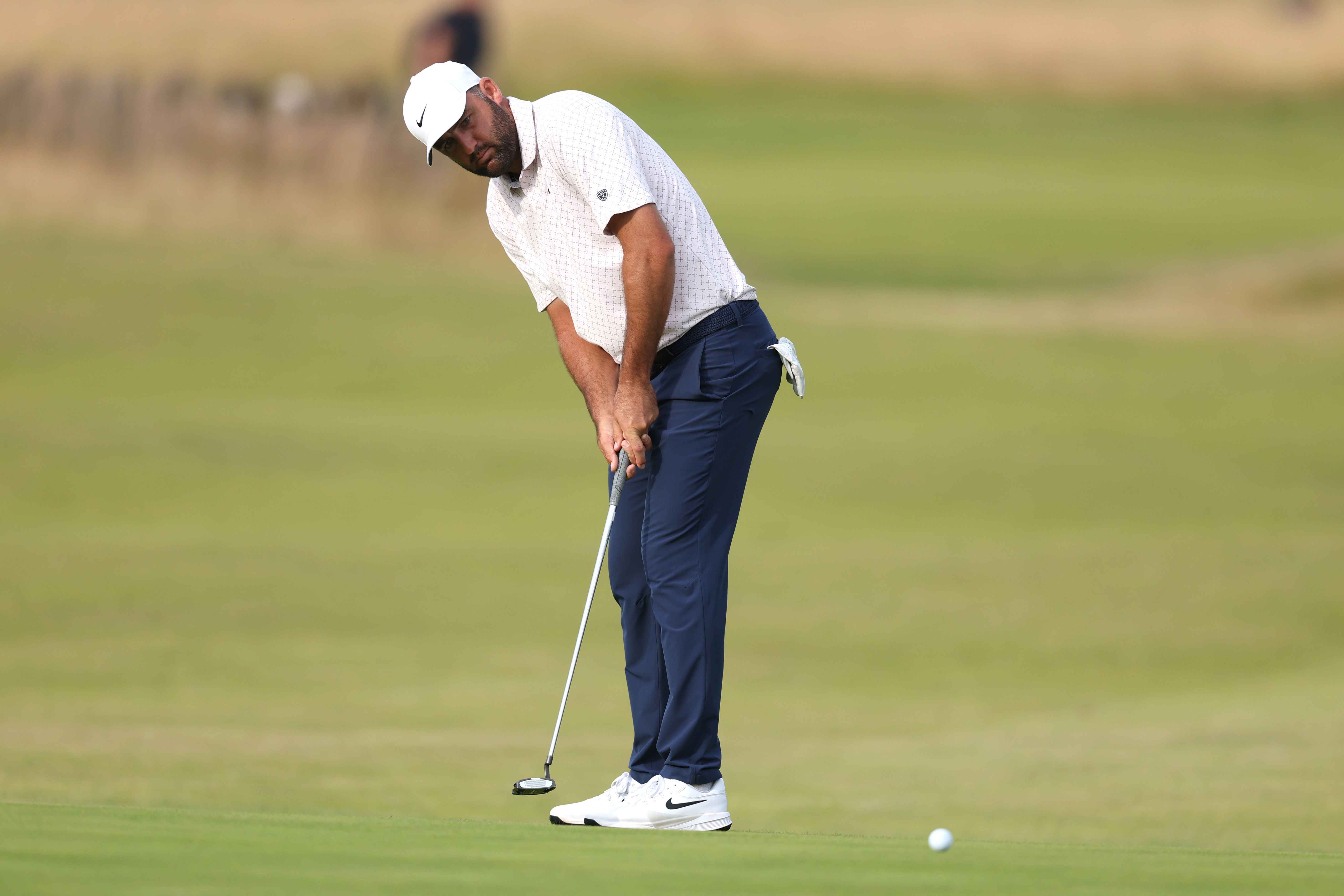A golfer in a white shirt and dark pants lines up a putt on a green.