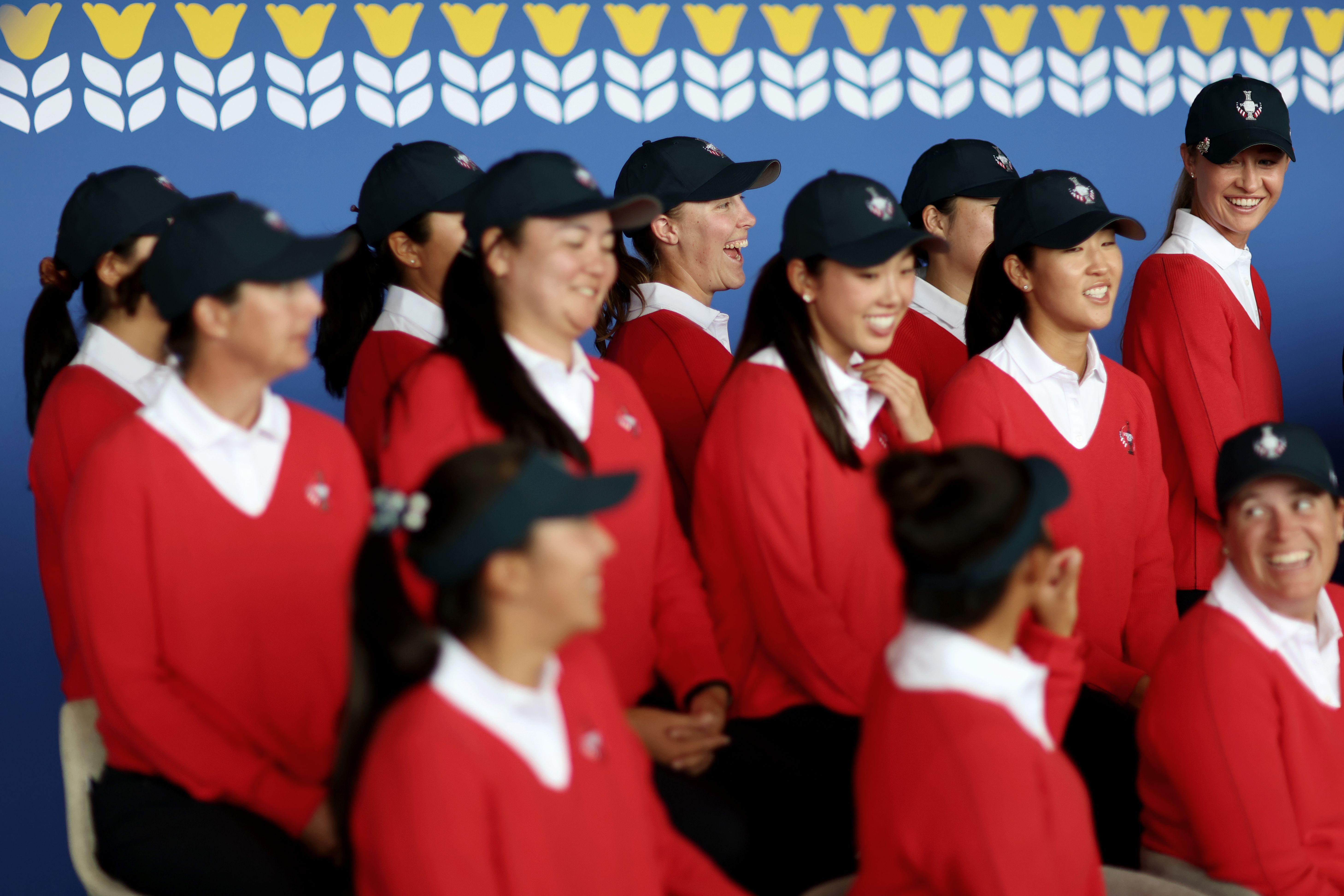 A group of smiling women in matching red sweaters and dark caps stand together.