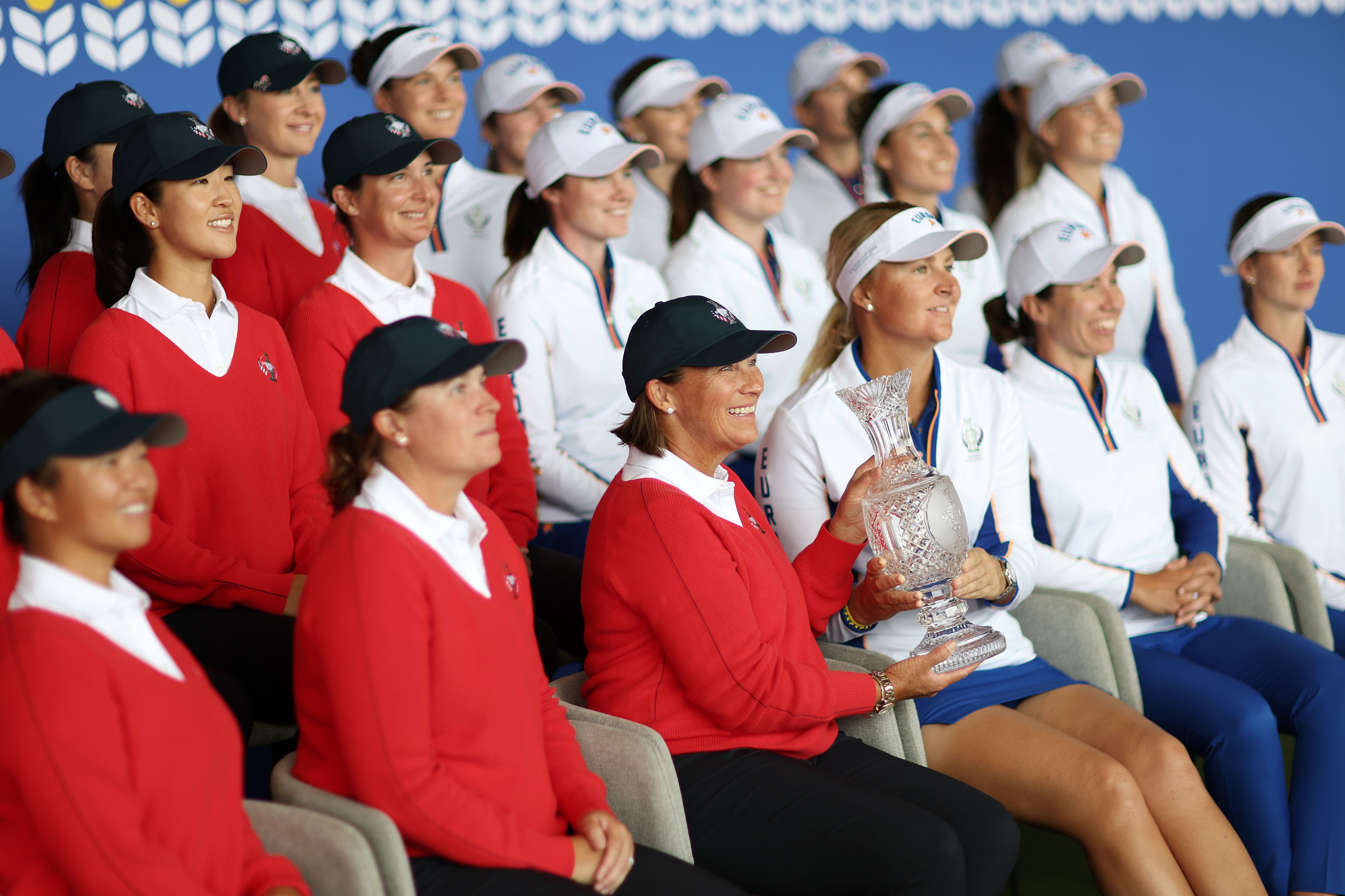 A group of female athletes, some in red, some in white, pose with a trophy.