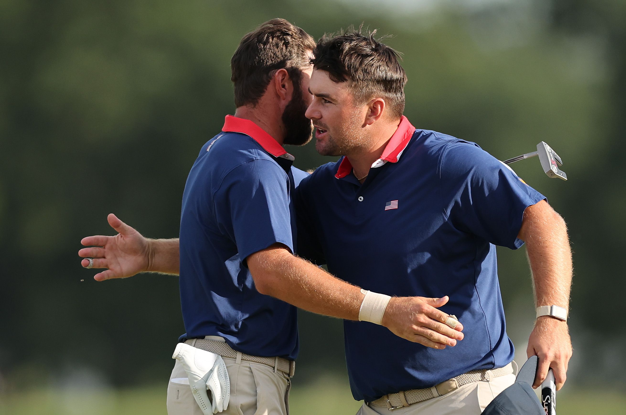 Two male golfers in blue shirts embrace on a sunlit golf course.