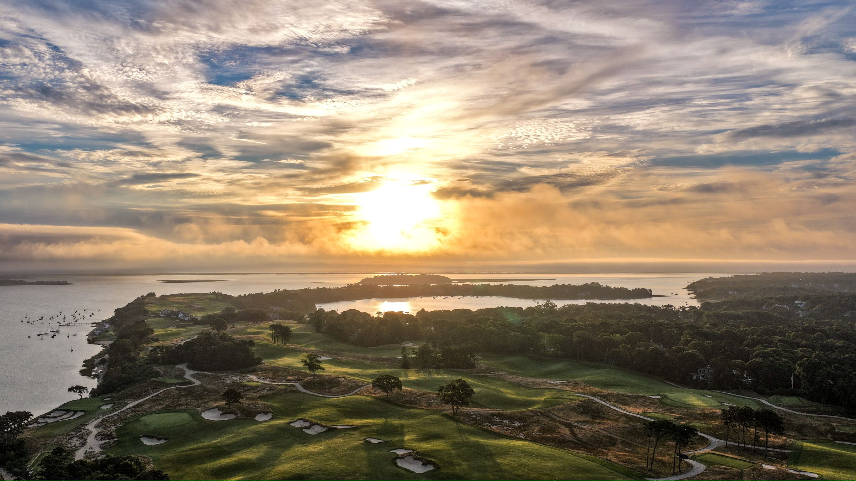 Aerial view of a vibrant sunset over a wide body of water and lush green land.