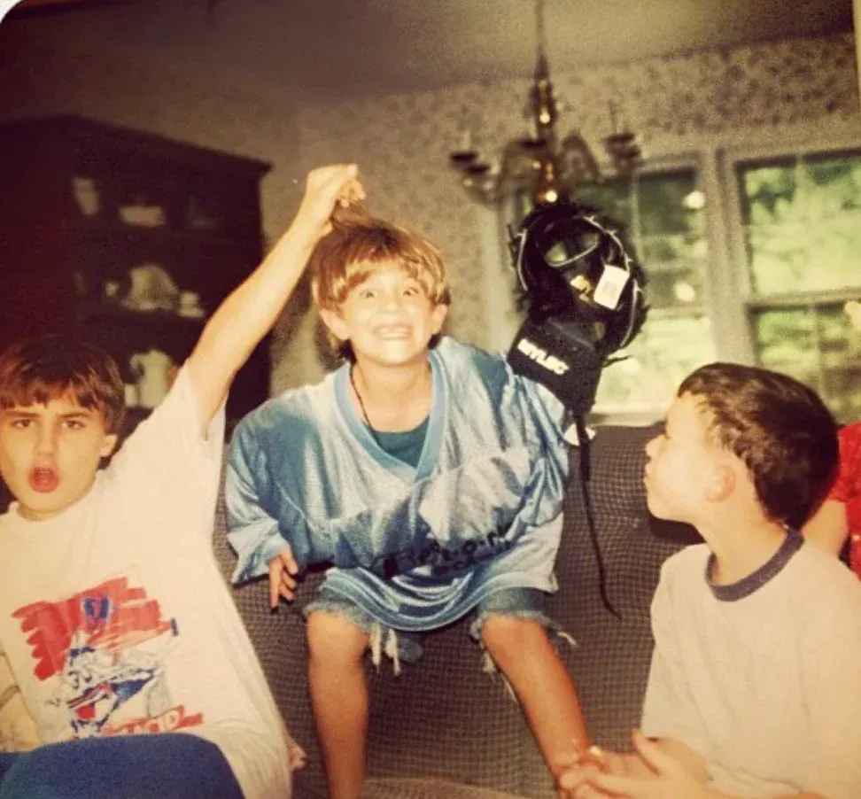 Three boys play indoors; one pulls hair, another smiles holding a dark object.