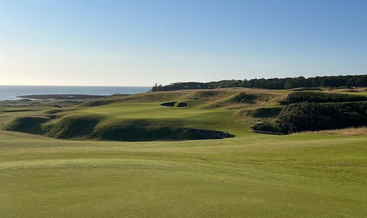 Expansive green golf course fairways bordered by coastal cliffs and a clear blue ocean.