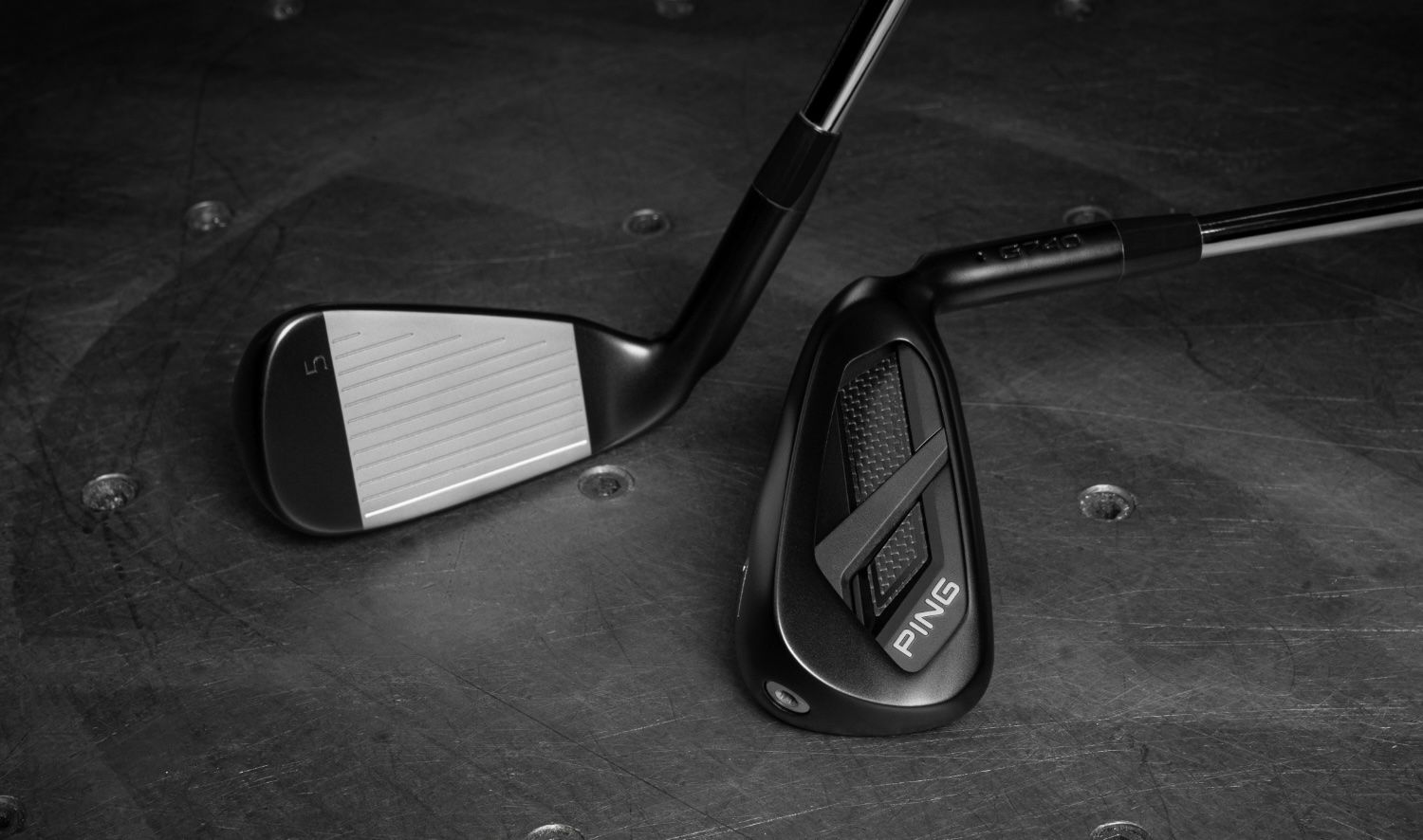 Two black and white golf club heads, one face up, on a dark textured surface.