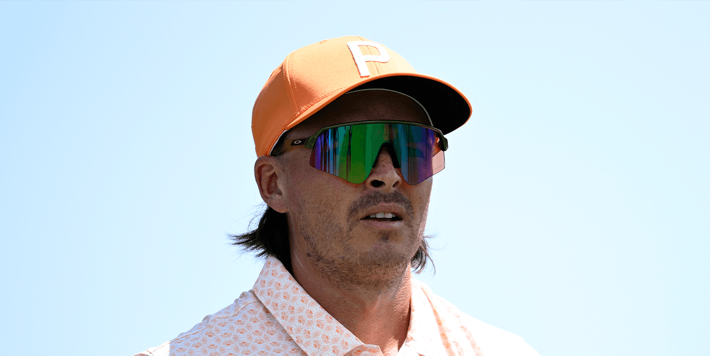 Man in orange cap and reflective rainbow sunglasses looking right under a bright blue sky.
