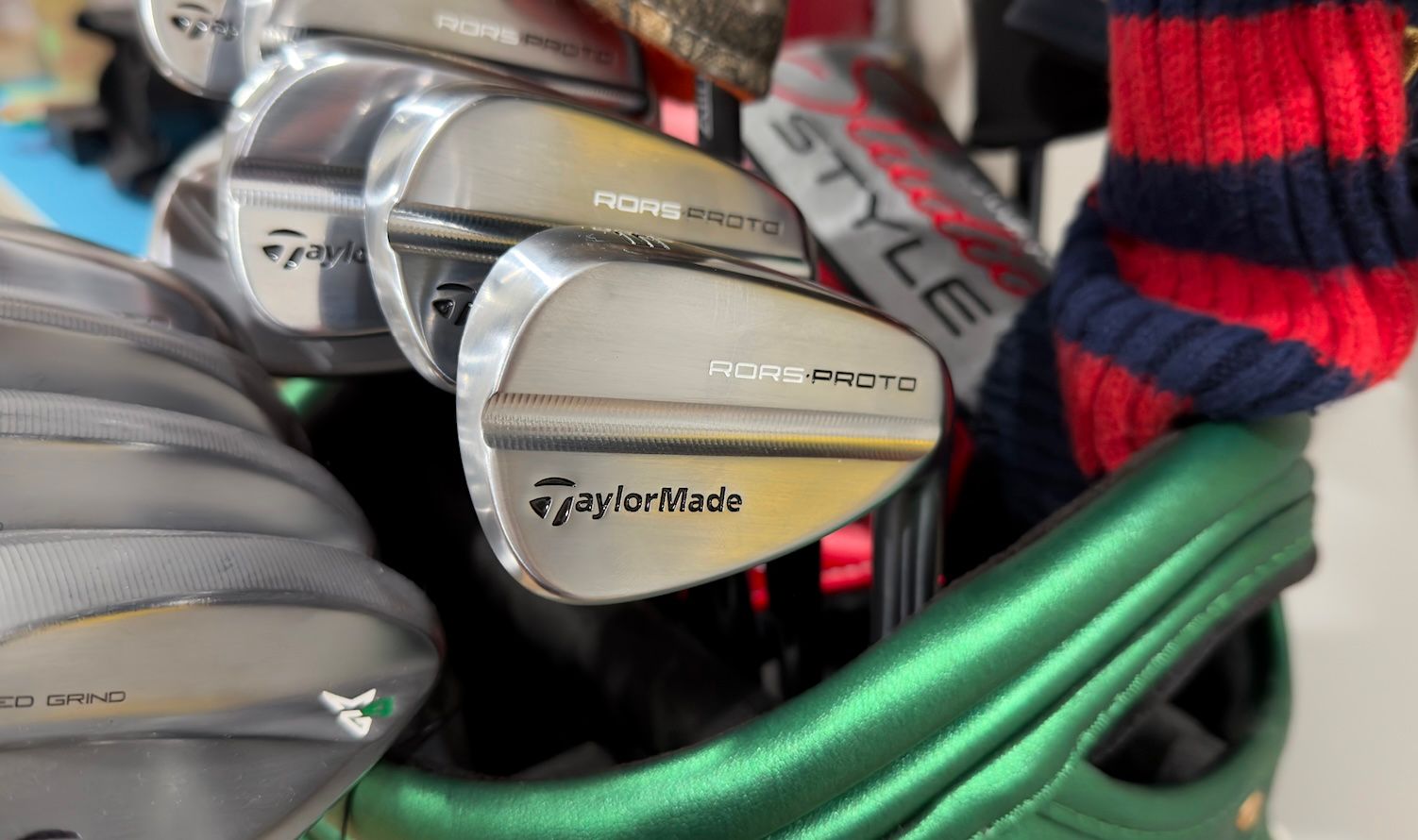 Close-up of TaylorMade golf wedges stored neatly in a green golf bag with a striped headcover.