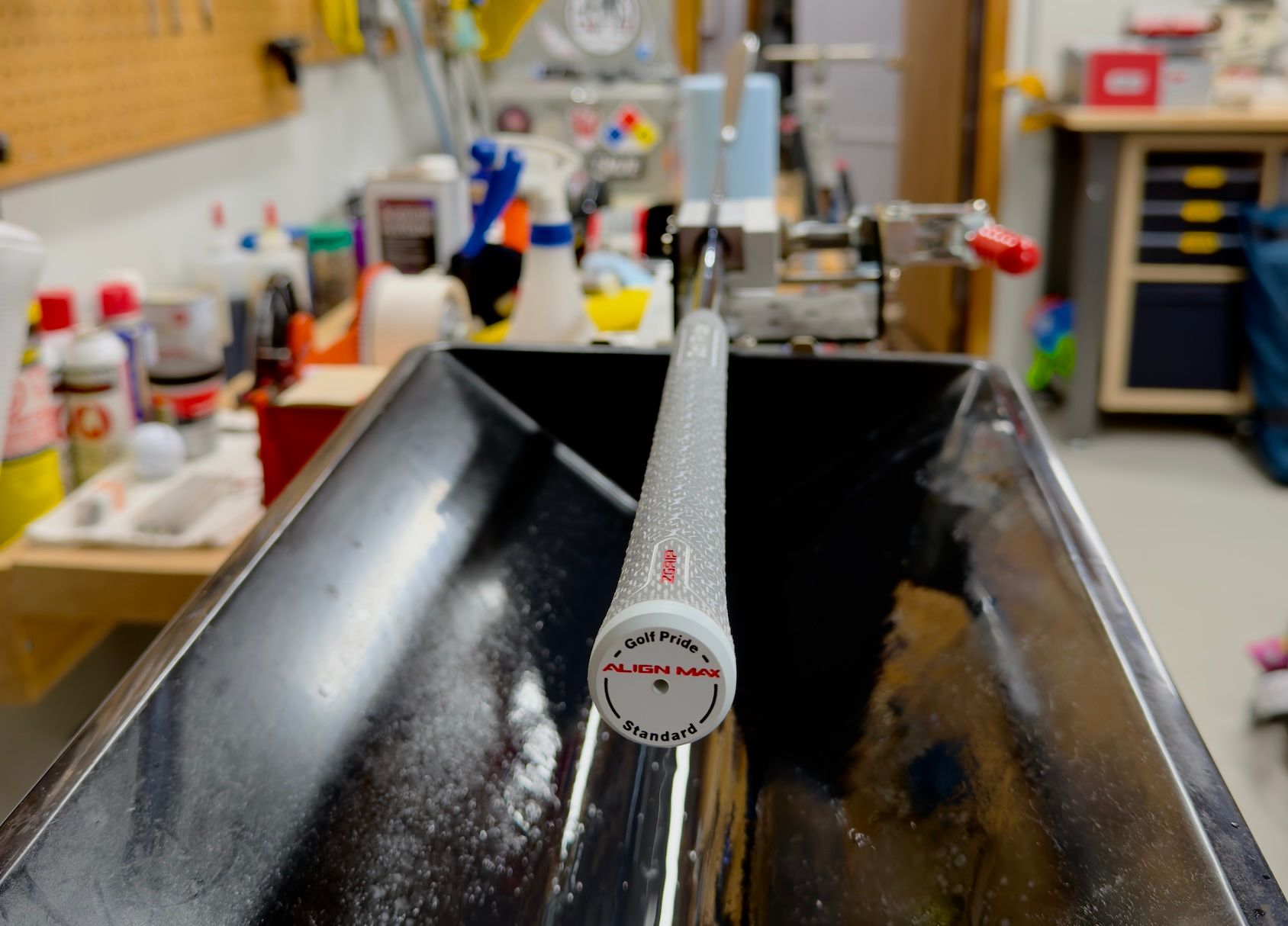 White golf club grip with a red Titleist logo resting in a dark metal trough.
