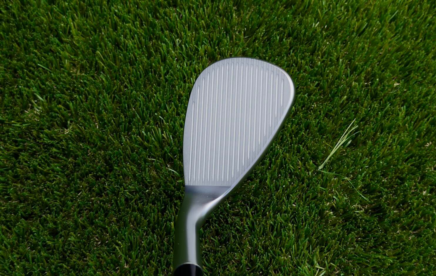 Close-up of a clean, silver golf wedge head resting on vibrant green grass.