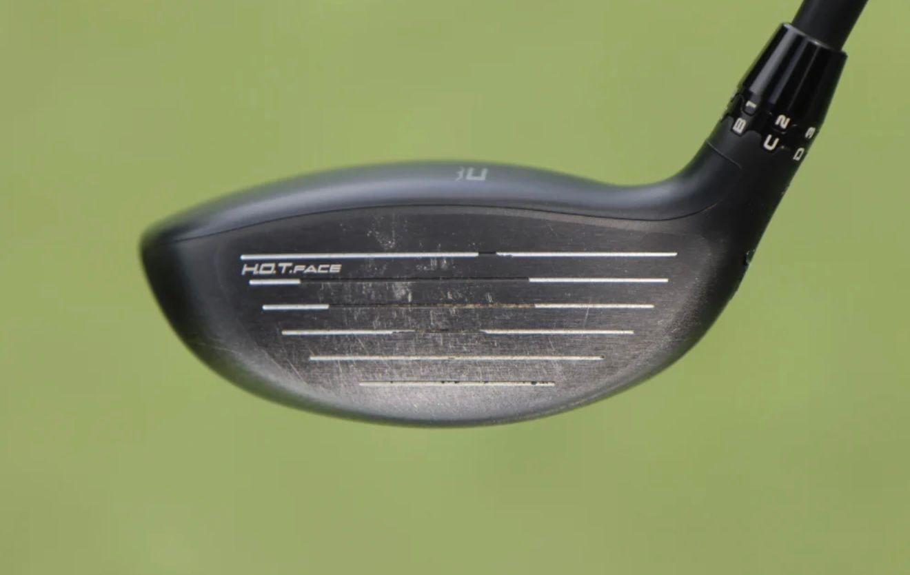 Close-up of a TaylorMade M3 golf club face with grooves against a green background.