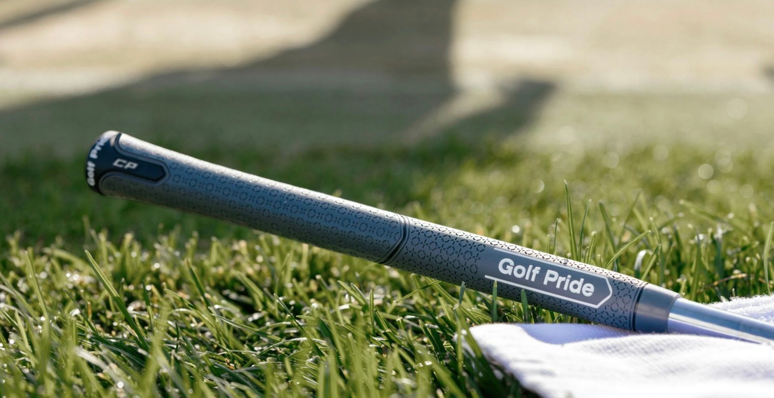 Close-up of a Golf Pride golf club grip resting on lush green grass.