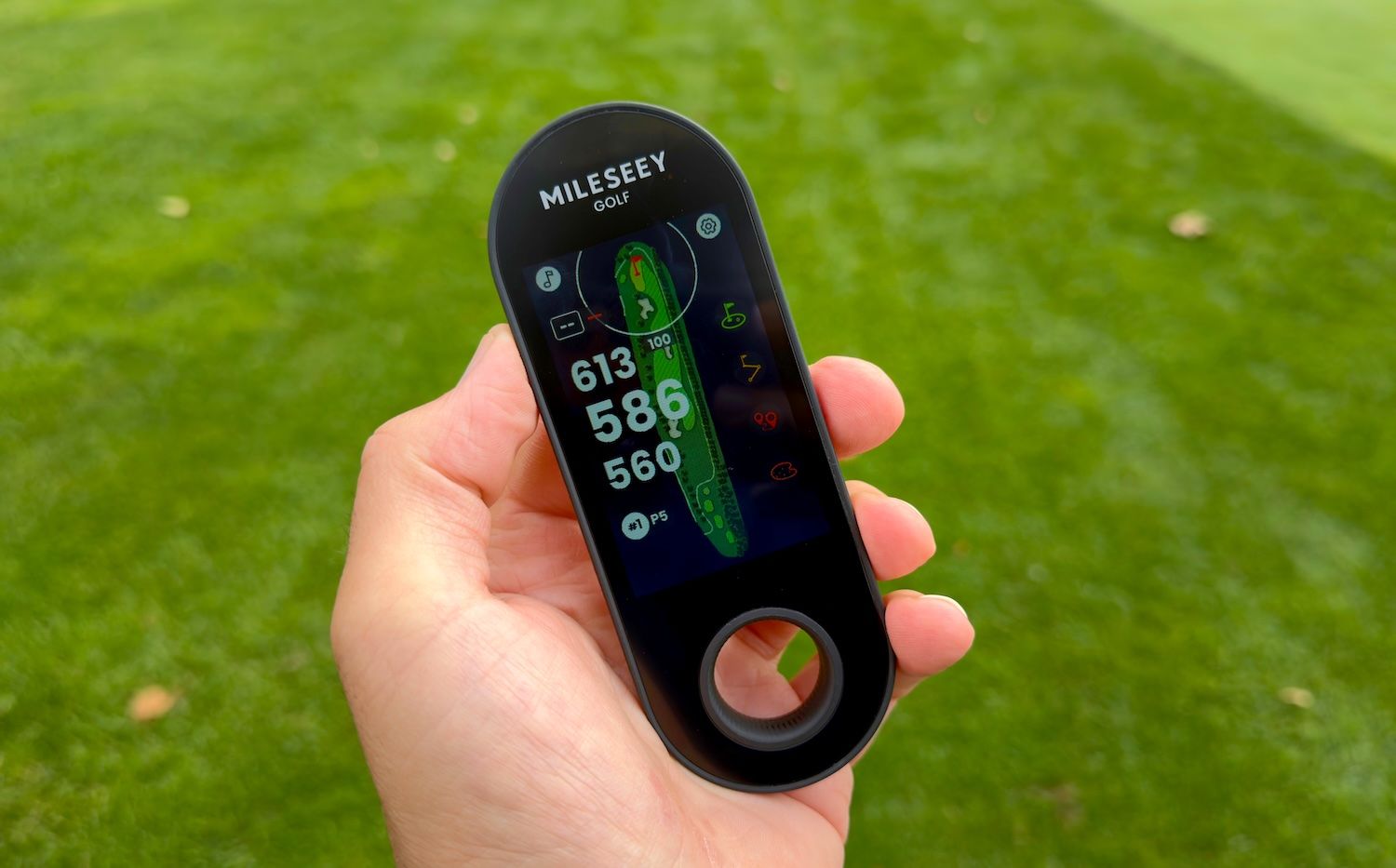 Hand holding a black golf GPS device displaying course layout and distances.