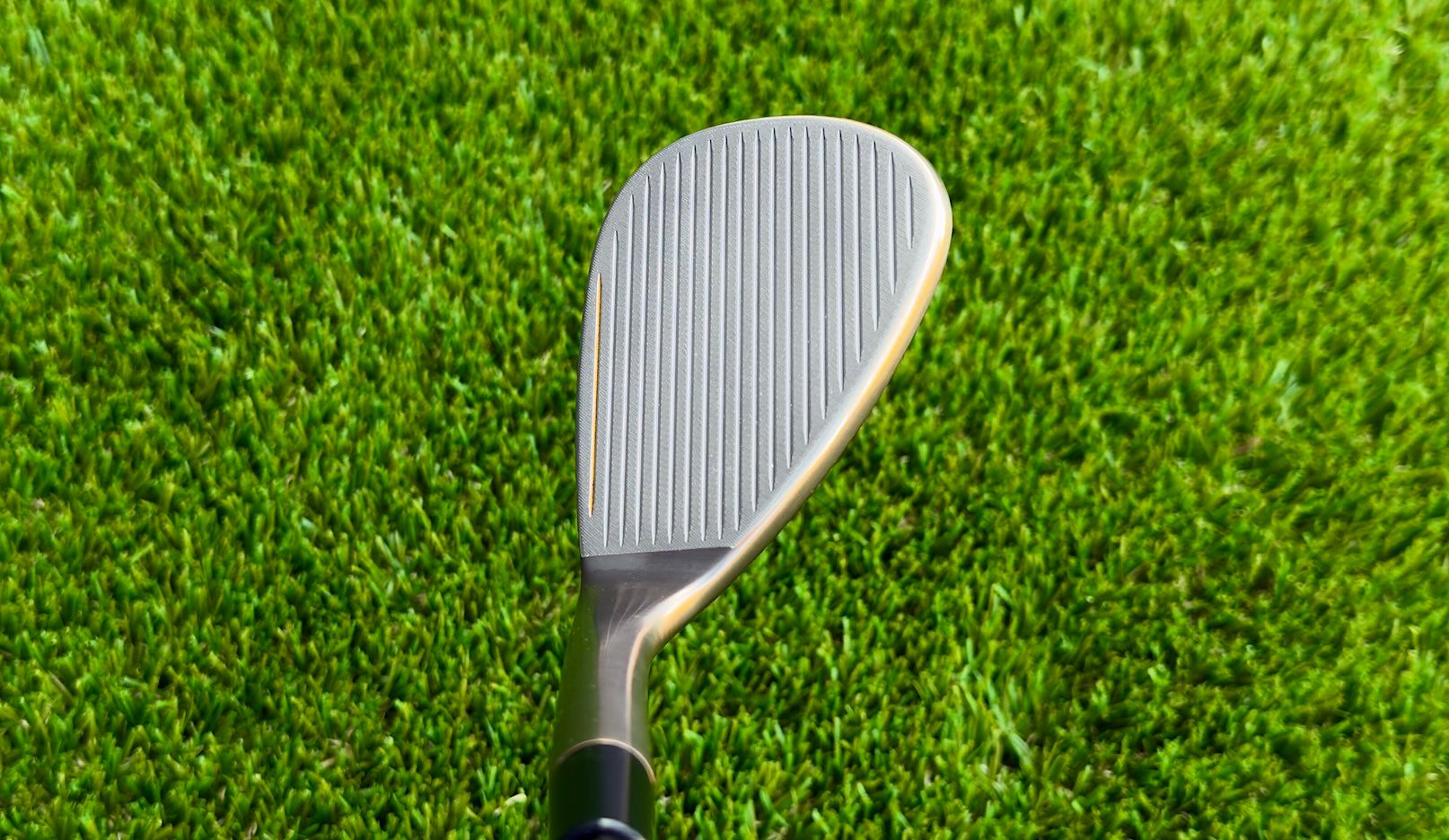 Golf club wedge face with grooves resting on vibrant green grass.