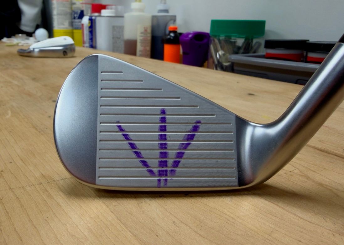 Golf club iron face with purple markings for swing analysis on a wooden table.