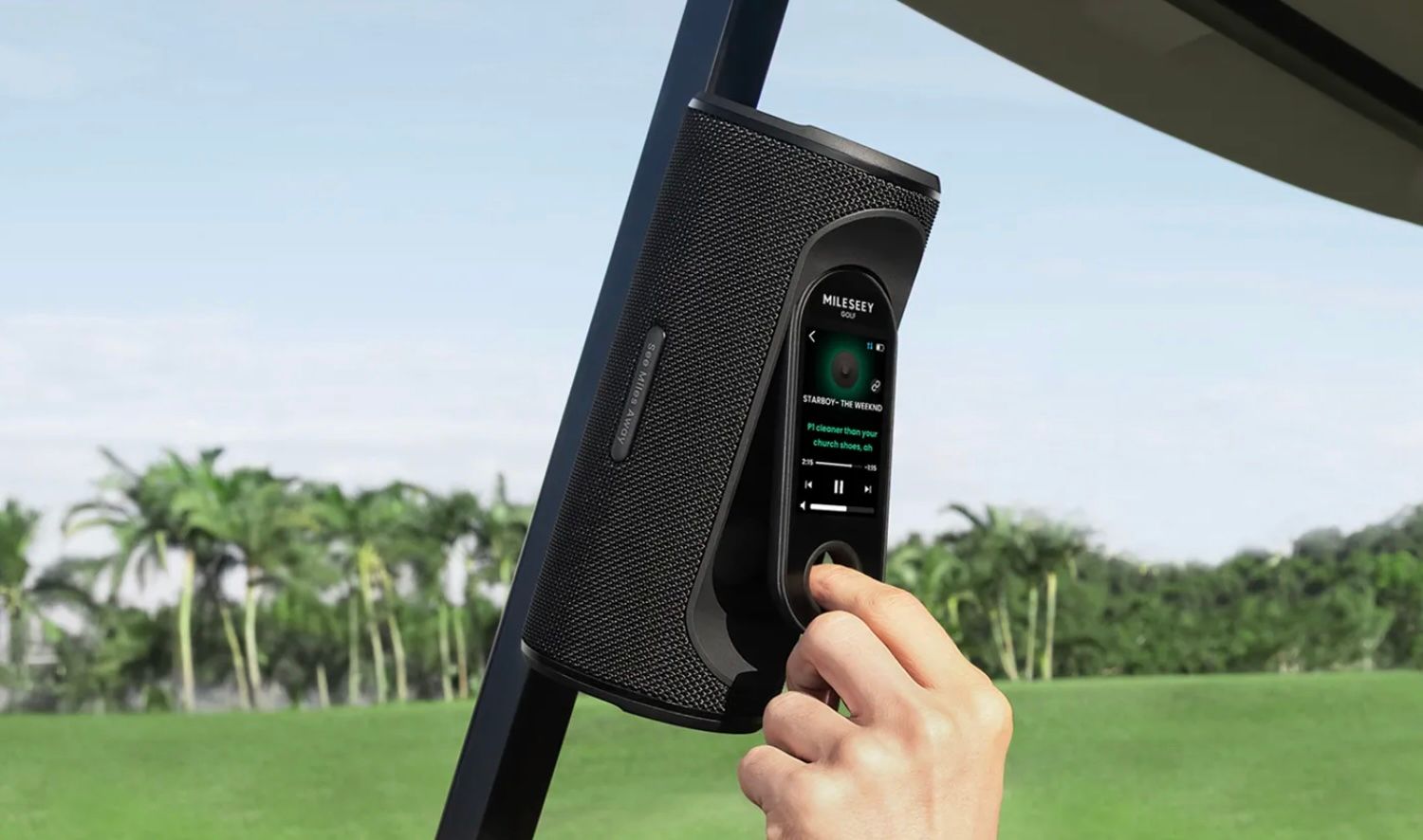 A hand adjusts settings on a golf cart's digital control panel on a sunny course.