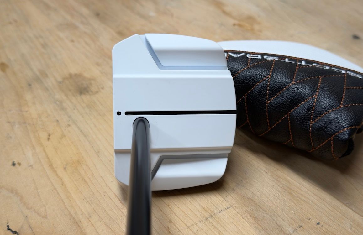 A white plastic object is being pried open with a black tool on a wooden surface.