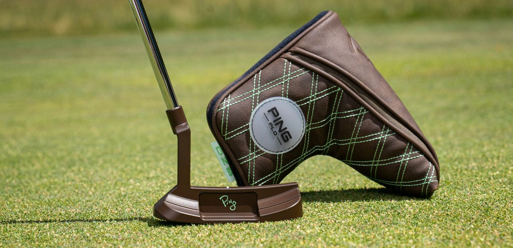 A brown golf putter and its camouflage headcover resting on vibrant green grass.