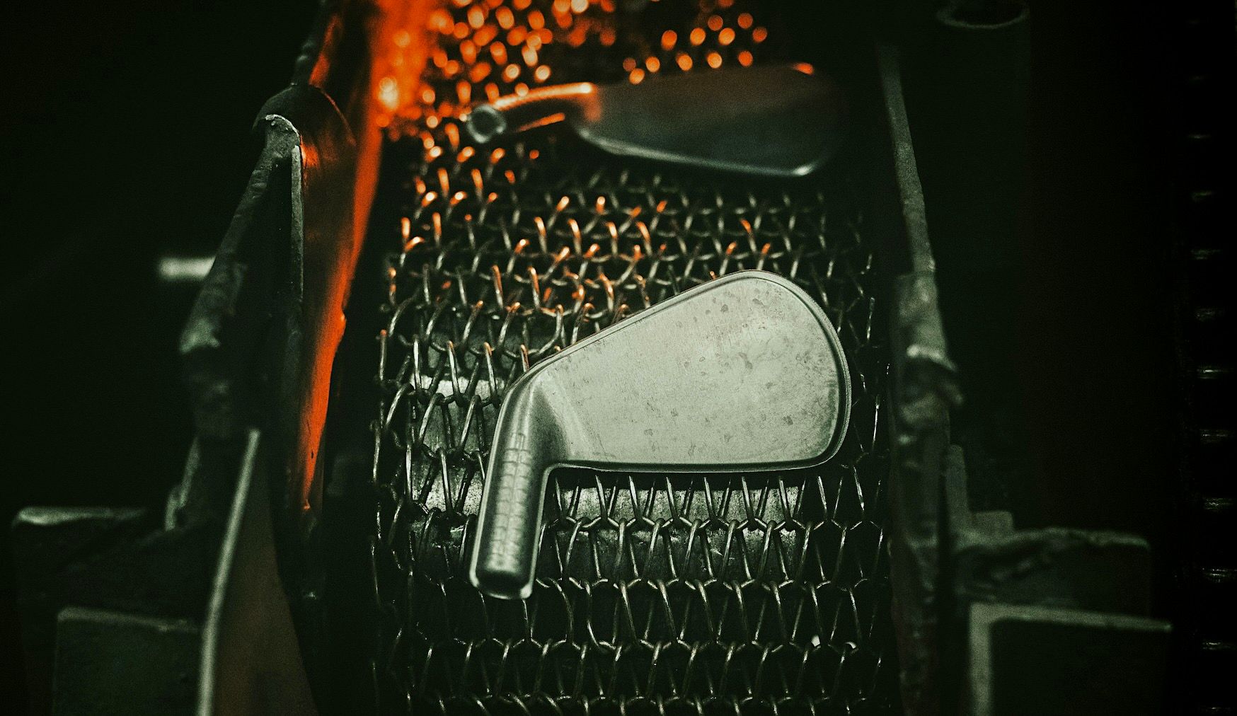 A golf club iron rests on a heated, glowing honeycomb metal surface.