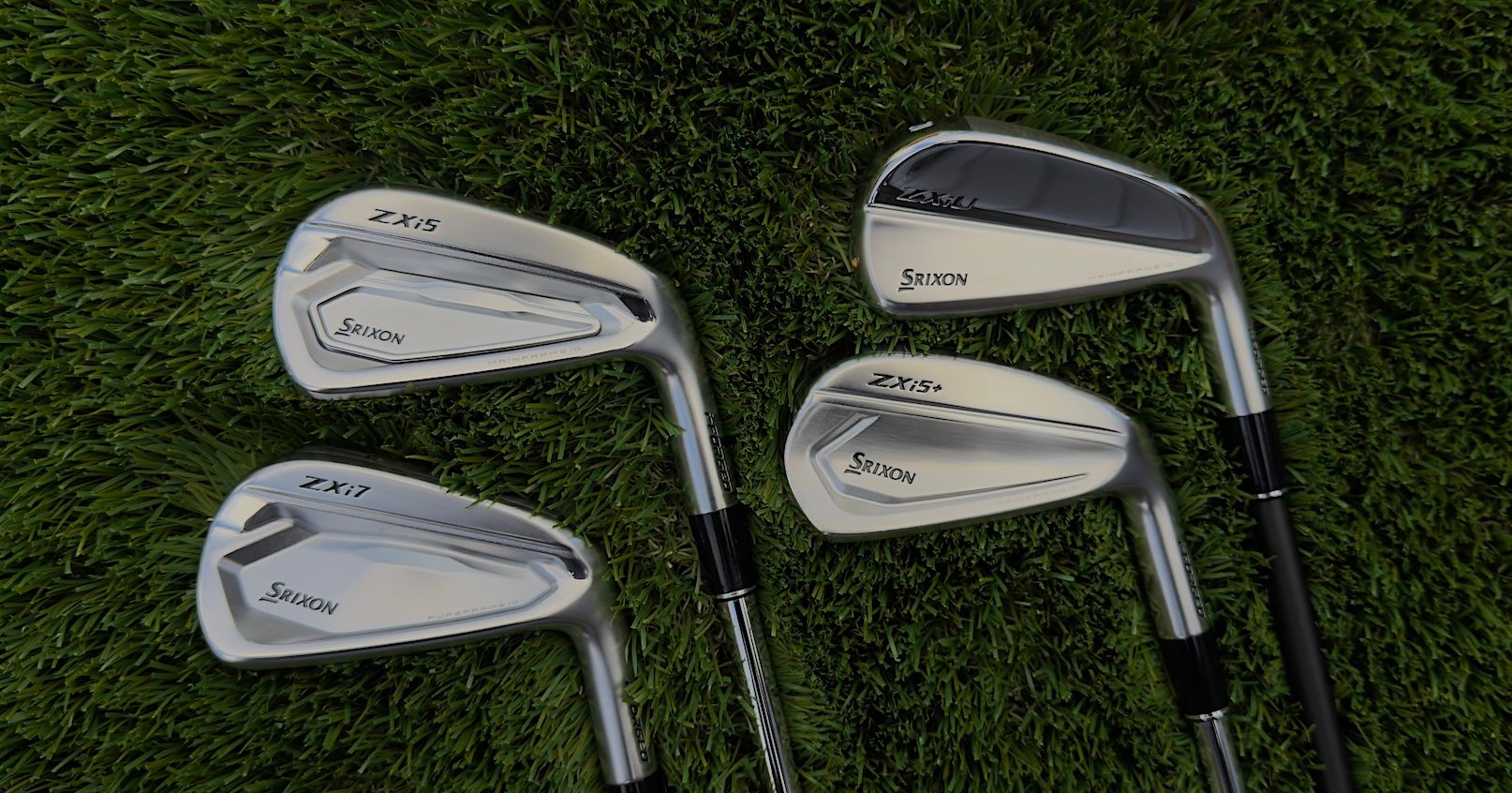 Four modern golf club irons resting on lush green grass.